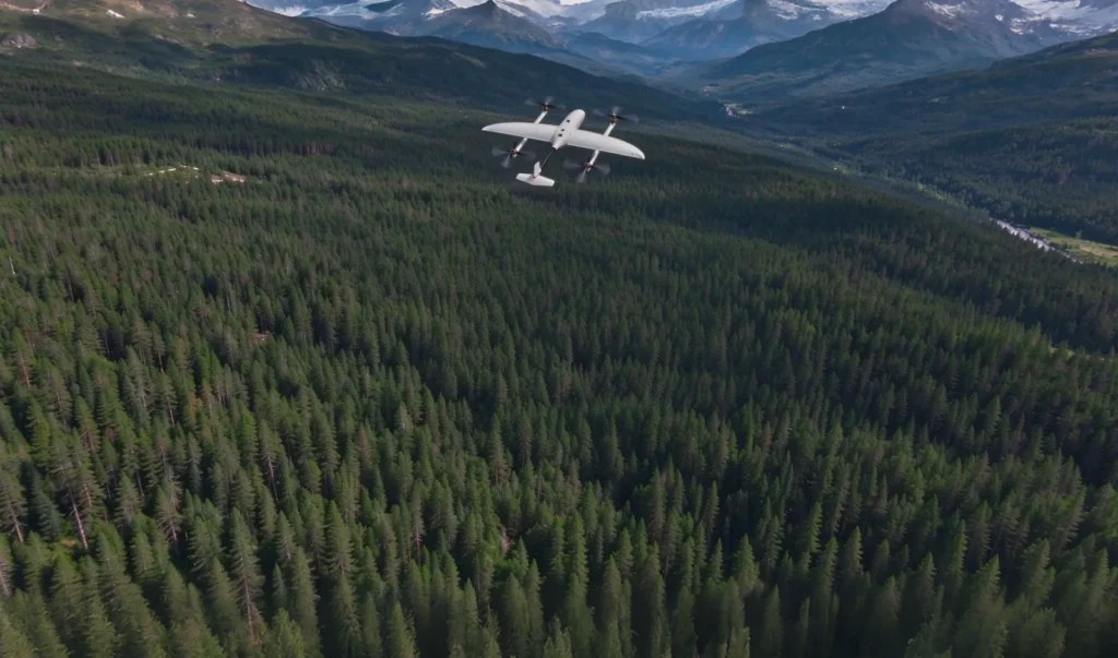 VTOL fixed-wing drone flying over a forest valley on battery power